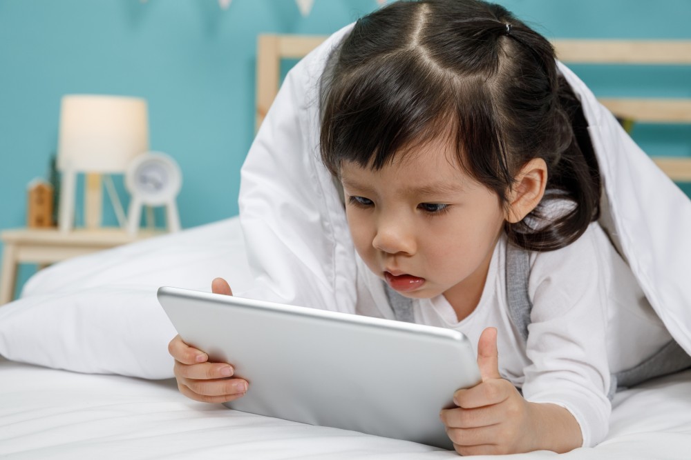 asian kids playing tablet on bed.