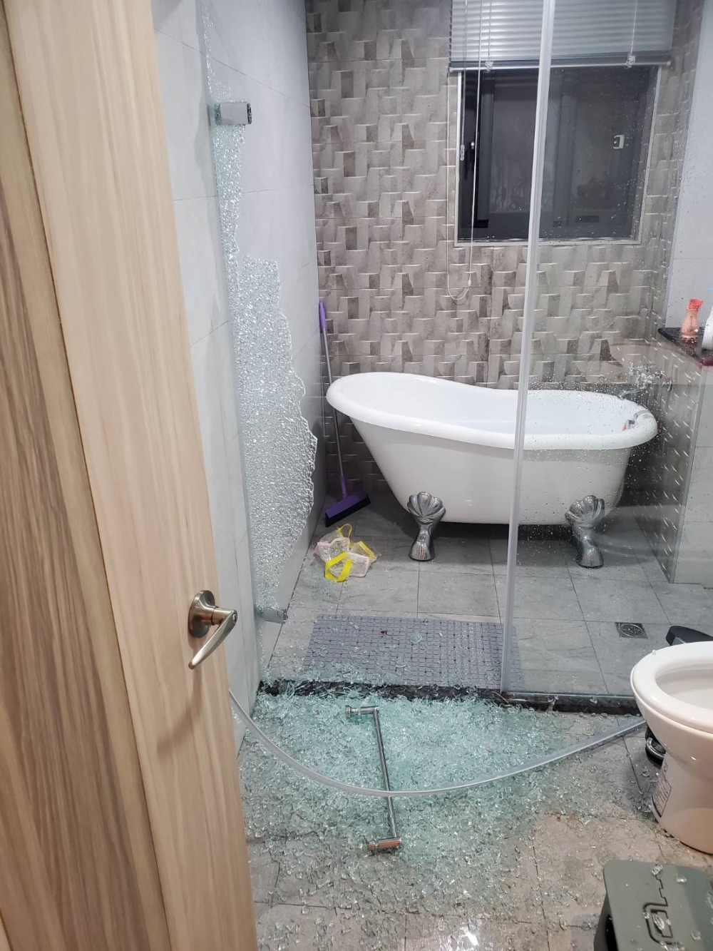 浴室玻璃門的碎片散落一地，嚇壞眾人。