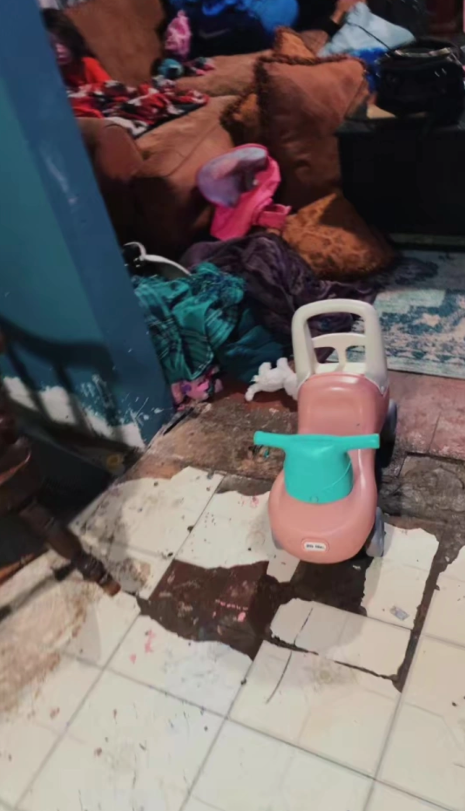 客廳環境相當混亂，在破爛的地板上有一架兒童玩具車。